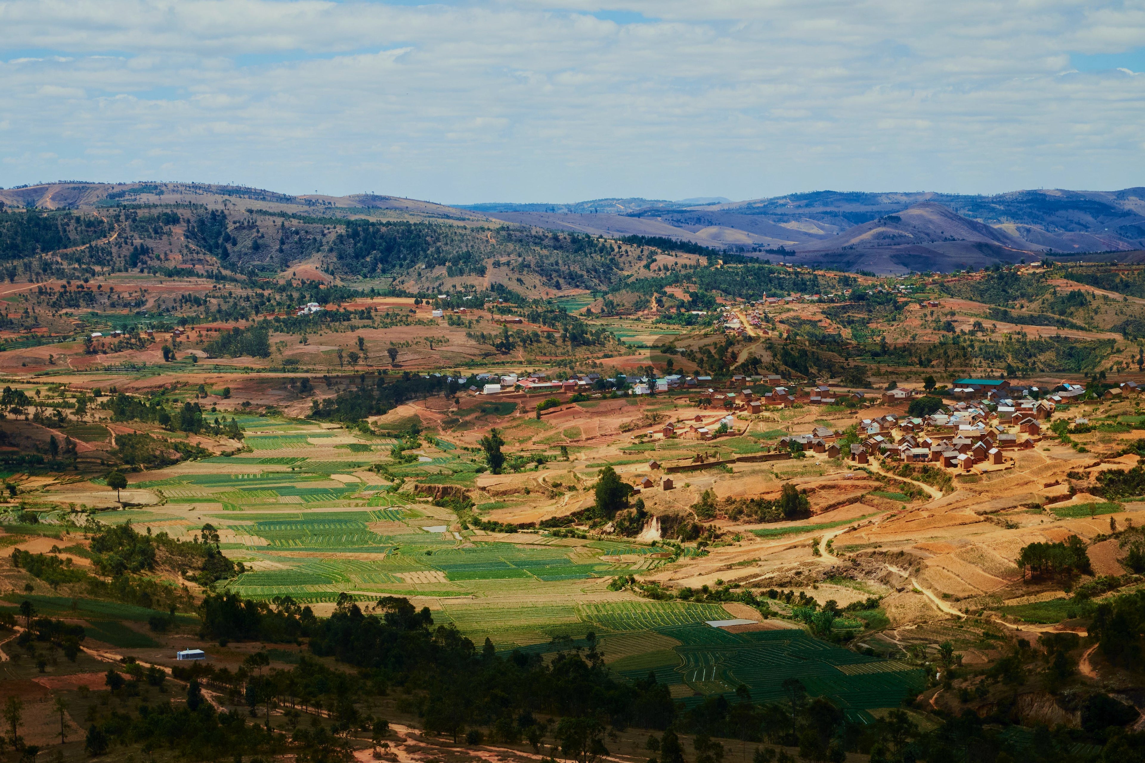 Scenic view of a rural landscape with fields and small buildings under a blue sky.
